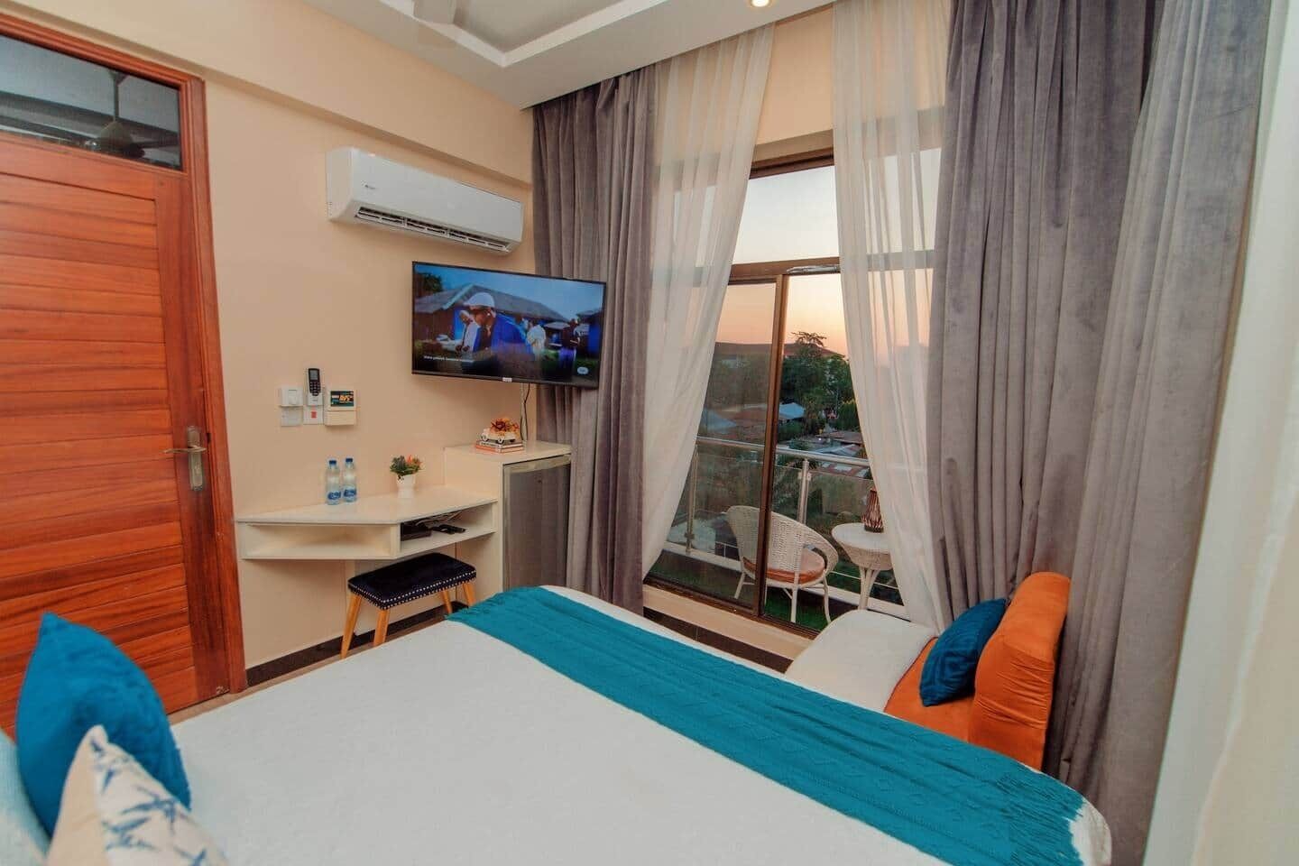 Ein Hotelzimmer mit Bett, Fernseher, Schreibtisch und einem fenster mit Vorhängen.