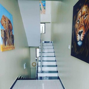 A staircase with glass railings leading to a landing, flanked by two large paintings, one of elephants and one of a lion. - The Retreat - Private Apt - Wi-Fi -Near shopping (Dar es Salaam)