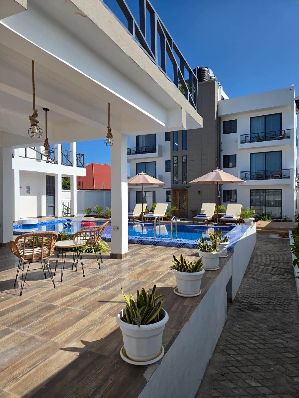A rooftop pool area with lounge chairs and umbrellas, surrounded by a modern building with balconies.