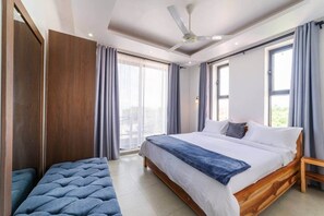 A bedroom with a large bed, a bench, a ceiling fan, and a view through the window. - Private 1 BDR Apt| w/Pool | Beachwalk - Generator (Jambiani)