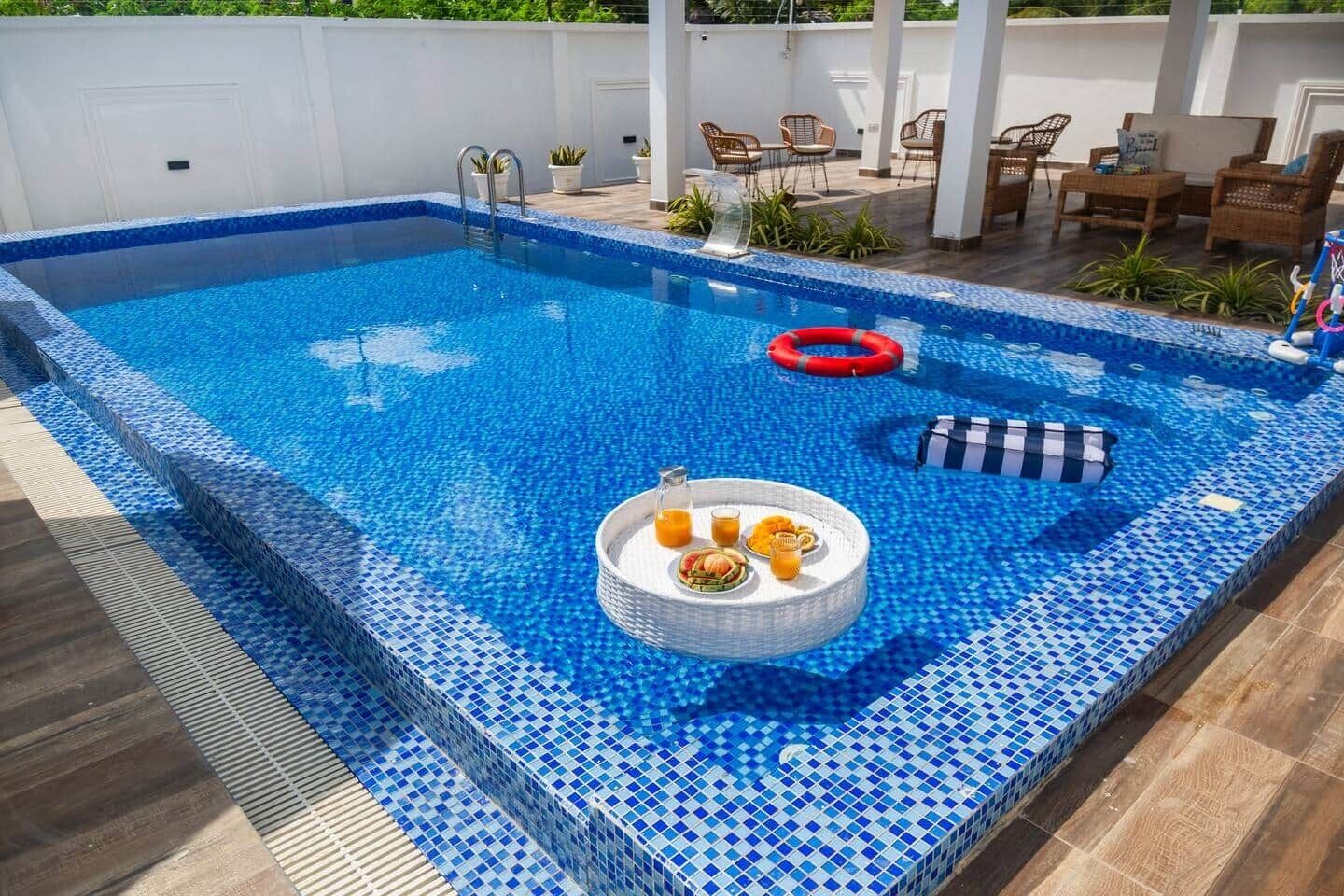 A rectangular outdoor swimming pool with a tiled edge, a floating platform with drinks, and lounge chairs.