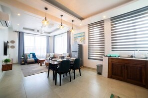 A modern living room with a dining area, a kitchen with a sink, and a large window with blinds. - Private 1 BDR Apt| w/Pool | Beachwalk - Generator (Jambiani)