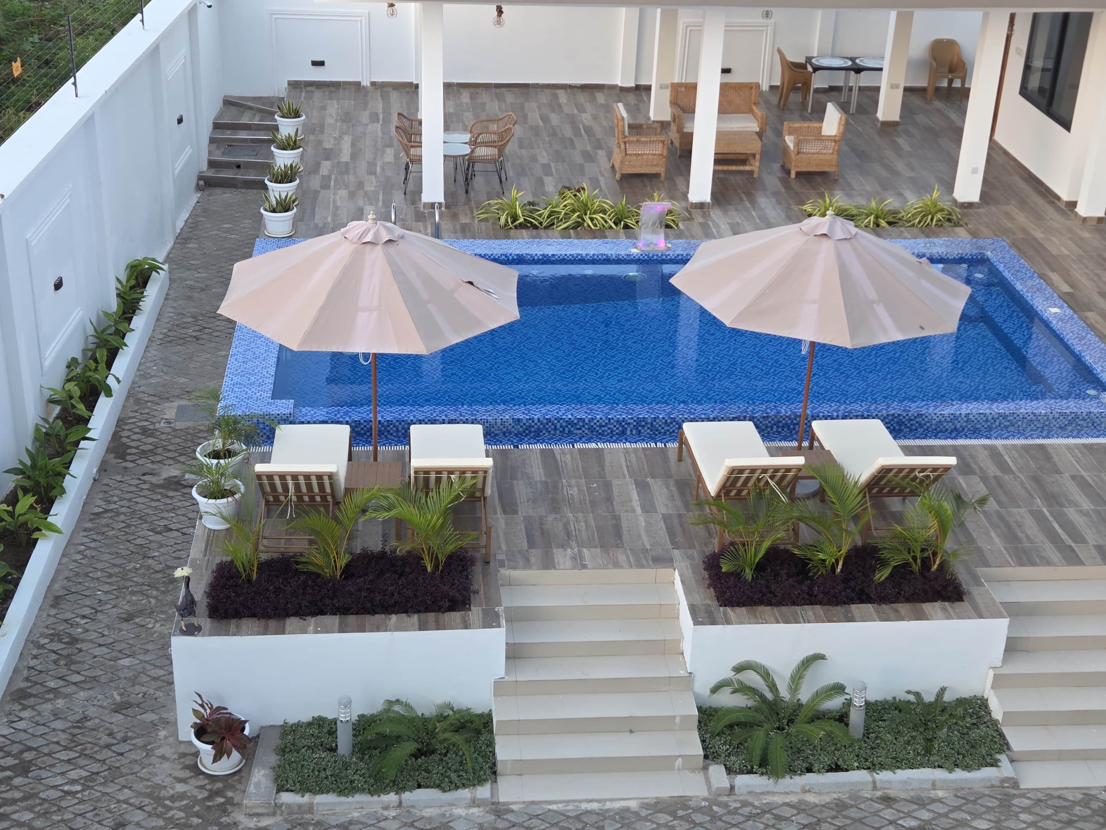 Une piscine avec deux parasols, des chaises longues et des plantes en pot.