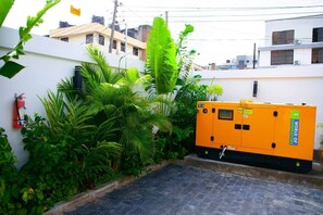 A building with a fire extinguisher mounted on the wall, surrounded by lush green plants. - New Urban Oasis Apt w/Pool + Hot tub + Gym (Dar es Salaam)