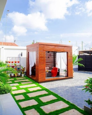 A wooden structure with a seating area, surrounded by a paved walkway and potted plants. - New Urban Oasis Apt w/Pool + Hot tub + Gym (Dar es Salaam)