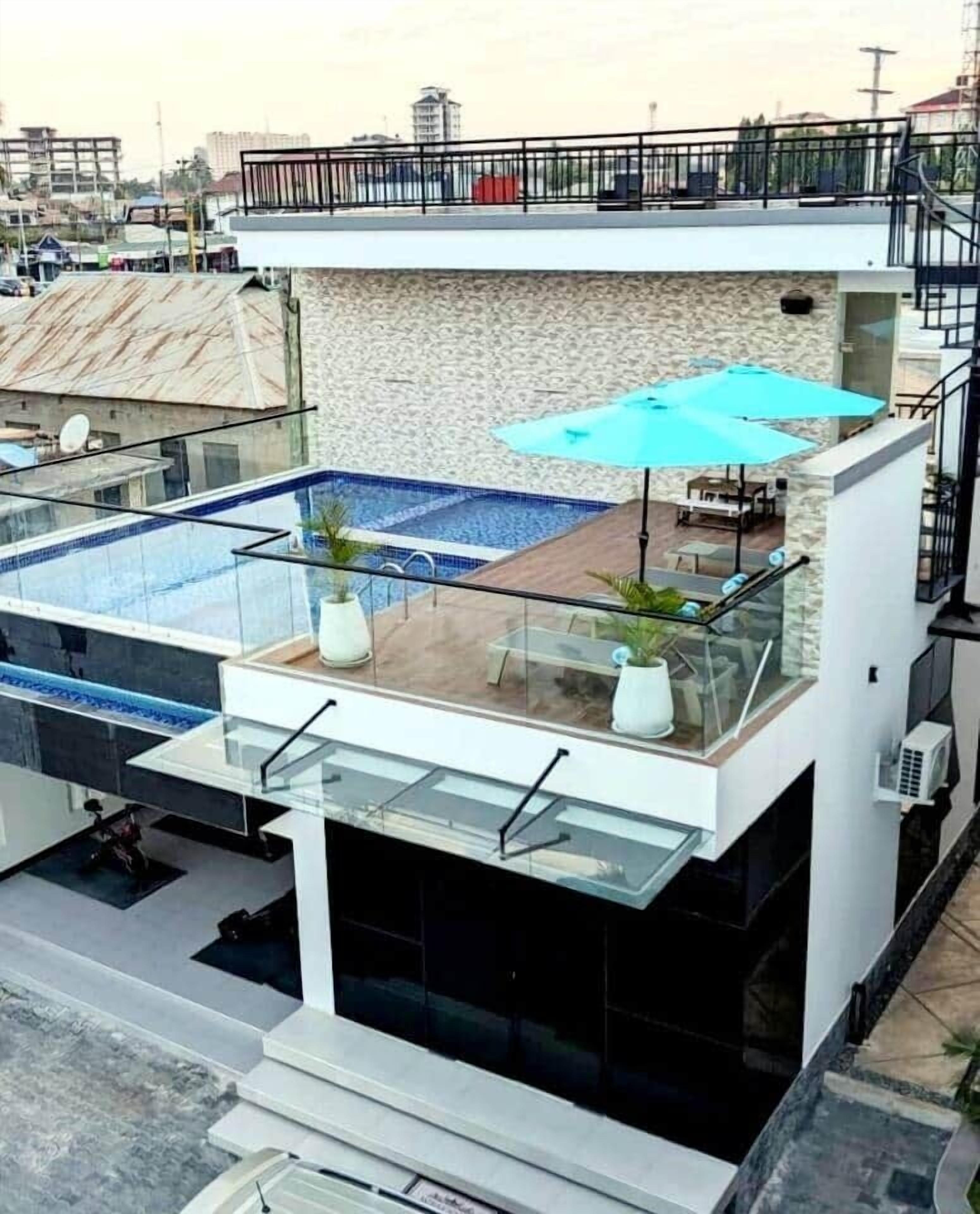 A modern building with a rooftop swimming pool, glass railings, and outdoor seating.