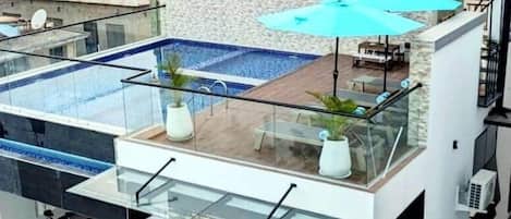 Un bâtiment moderne doté d’une piscine sur le toit, de rampes en verre et d’un espace extérieur aménagé pour s’asseoir.