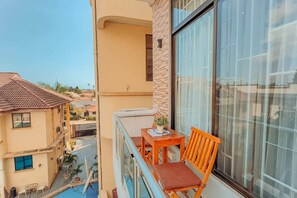 A balcony with a table and chair, a potted plant, and a view of neighboring buildings. - Serenity Peak Apt -King Bed - Kitchen-Laundry-Generator (Dar es Salaam)