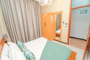 A hotel room with a bed, a wardrobe, a mirror, and a door leading to a bathroom. - Serenity Peak Apt -King Bed - Kitchen-Laundry-Generator (Dar es Salaam)
