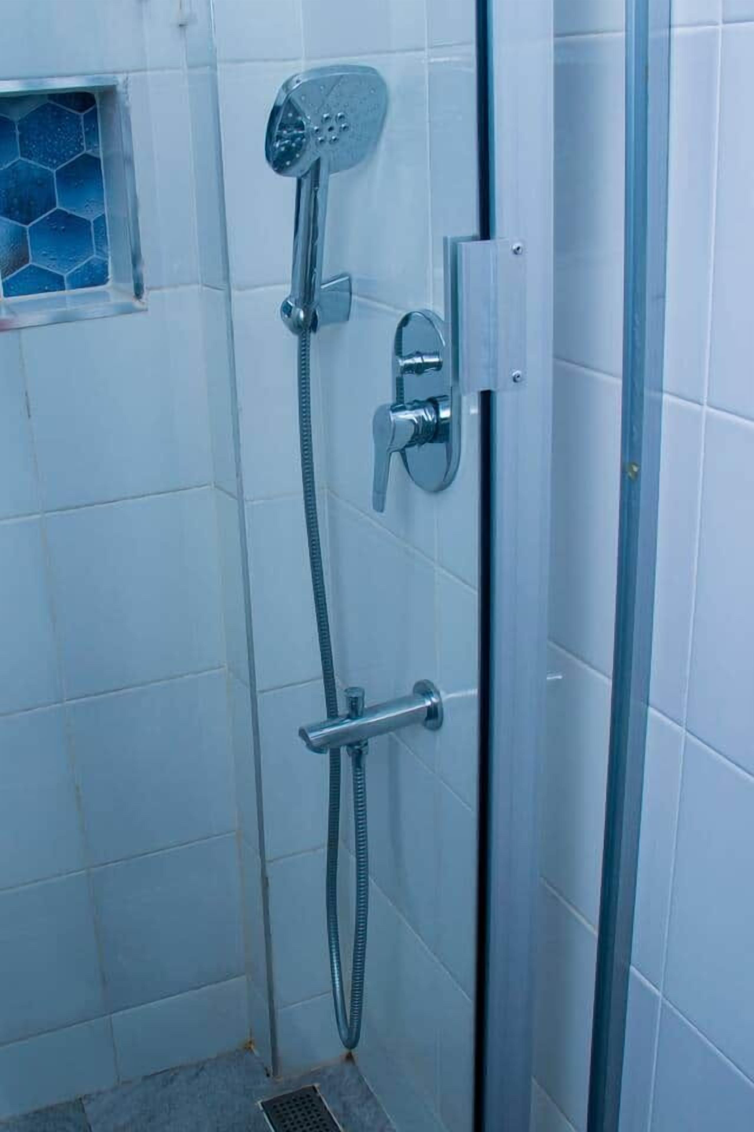Ein Badezimmer mit Duschkabine, Duschbrausehandstück und Wandarmatur.