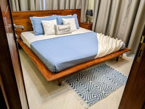 Ein Bett mit Holzrahmen, einer blauen Tagesdecke und einem gemusterten Teppich.