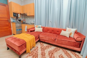 A compact living space with a sofa, a kitchen area, and a dining table. - Serenity Peak Apt -King Bed - Kitchen-Laundry-Generator (Dar es Salaam)