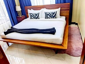 A bed with a wooden frame, white bedding, and two pillows with a black and white pattern. - The Hidden Charm- Private Apt- Wi-Fi-Easy access to town (Dar es Salaam)