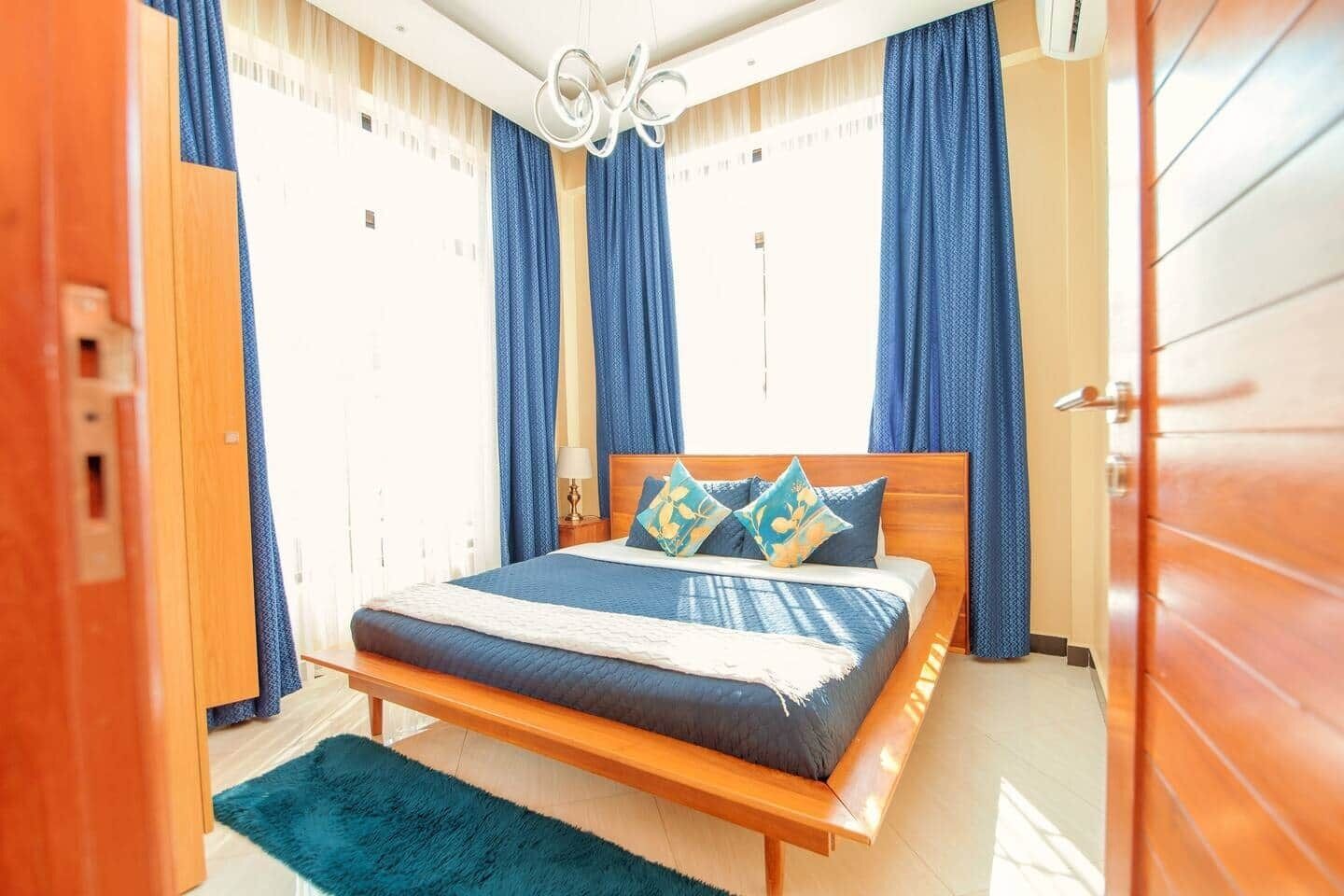 A bedroom with a wooden bed, blue curtains, and a fluffy rug.