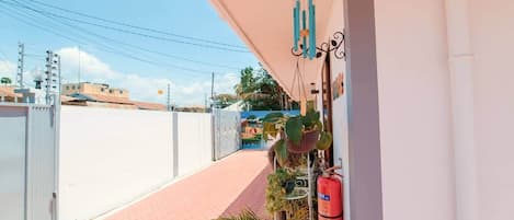 A balcony with a view of a street, a fire extinguisher, and hanging wind chimes.
