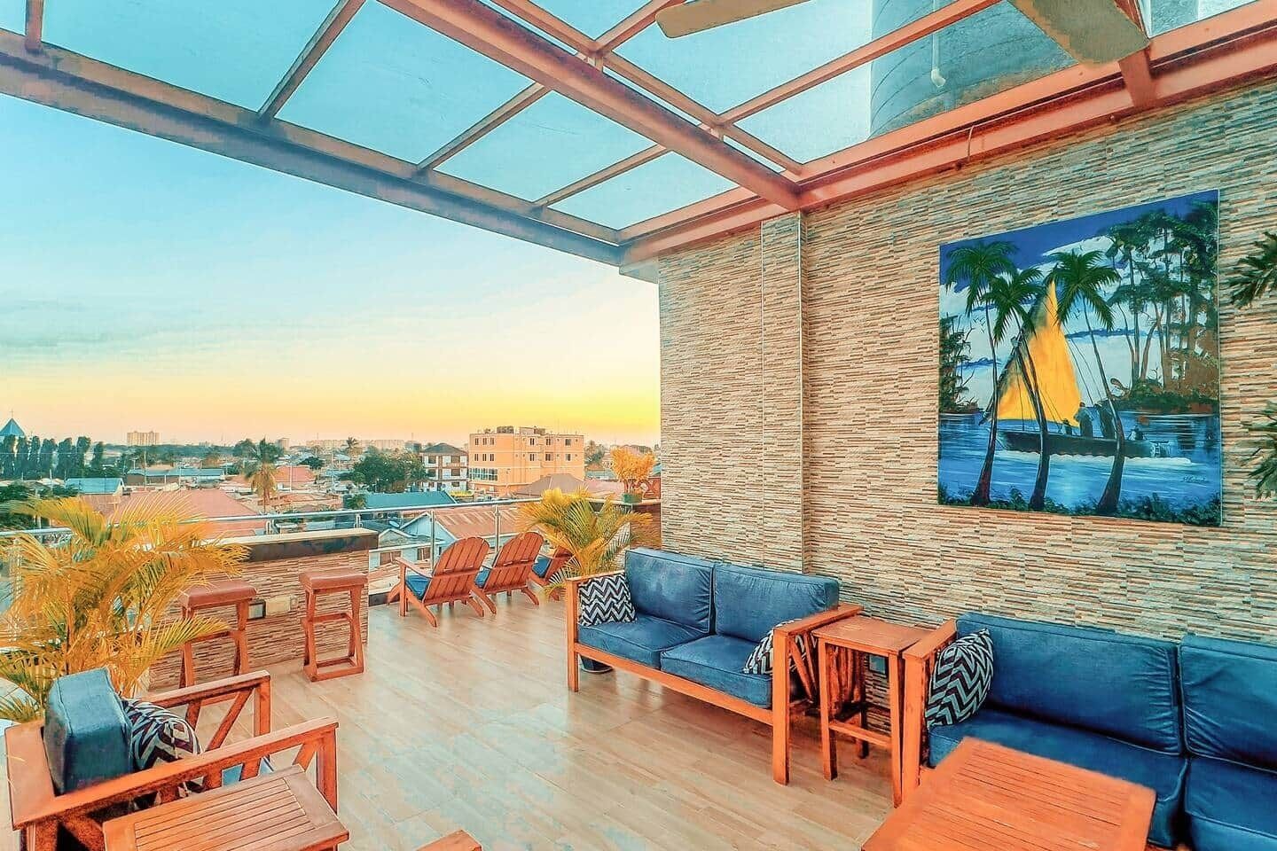 A rooftop terrace with a blue sofa, wooden chairs, and a painting of a sailboat.