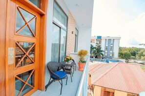 Ein Balkon mit Korbmöbeln, einem Blumentopf und Blick auf einen Swimmingpool und Gebäude.