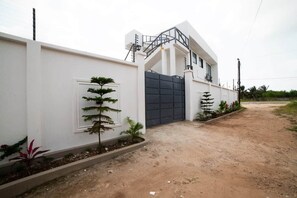 Un bâtiment moderne à l’extérieur blanc, doté d’une entrée sécurisée par un portail et d’une allée en terre.