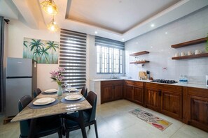 A modern kitchen with wooden cabinets, a built-in stove, and a dining area with a table set for two. - Seashells Private Apt - Kitchen| Pool |Wi-Fi | Beachwalk (Jambiani Kikadini)