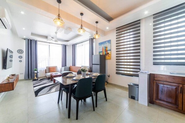 A modern living room with a dining area, large windows, and a kitchen. - Ocean Breeze retreat - 7 min Beach walk | Pool (Jambiani Kikadini)