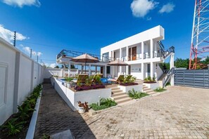 A modern building with a pool, outdoor seating, and a staircase leading to a balcony. - Ocean Breeze retreat - 7 min Beach walk | Pool (Jambiani Kikadini)