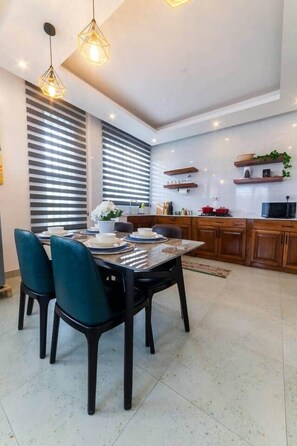 Cozinha moderna com área de jantar, incluindo mesa com cadeiras, iluminação pendente e prateleiras embutidas.