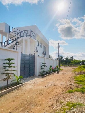 Uma casa moderna com dois andares, uma escadaria, portão e entrada de terra.