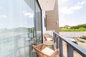 Ein Balkon mit Korbmöbeln und Blick auf Grünflächen und Gebäude.