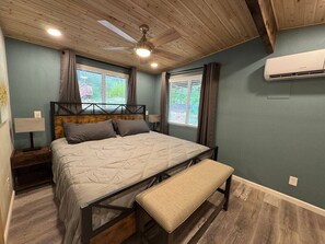 Ein Schlafzimmer mit einem Bett, einer Sitzbank, einem Deckenventilator und einer Klimaanlage.