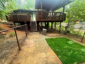 A wooden deck with a staircase leading to a covered area, surrounded by a chain-link fence. - Creekside Retreat | 2BR Hideaway + Private Hot Tub (Sedona)