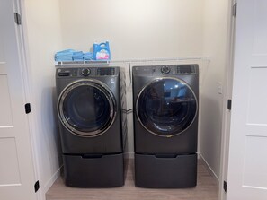 A laundry room with two front-loading washing machines and a shelf with laundry detergent.