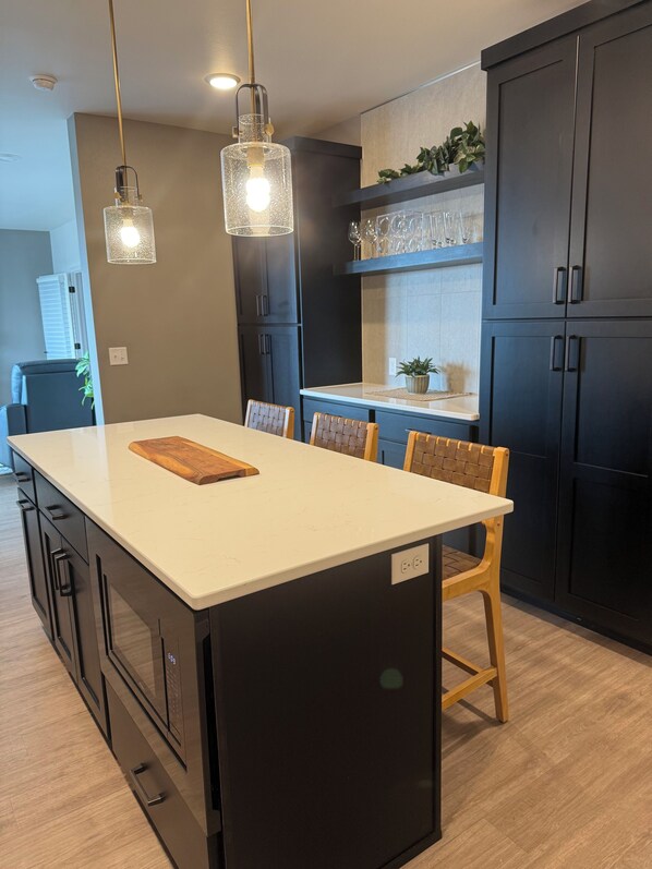 A modern kitchen with a central island, dark cabinetry, and pendant lighting.