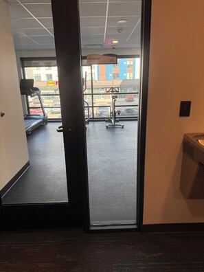 A gym with exercise equipment, a treadmill, and a view of the street outside.