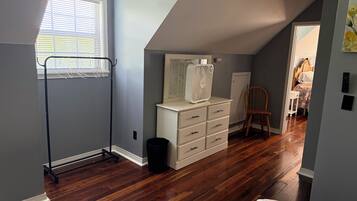 A room with a sloped ceiling, a white dresser, a wooden chair, and a window with blinds.