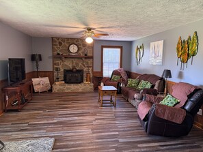 A living room with a stone fireplace, a sofa, a television, and a ceiling fan.