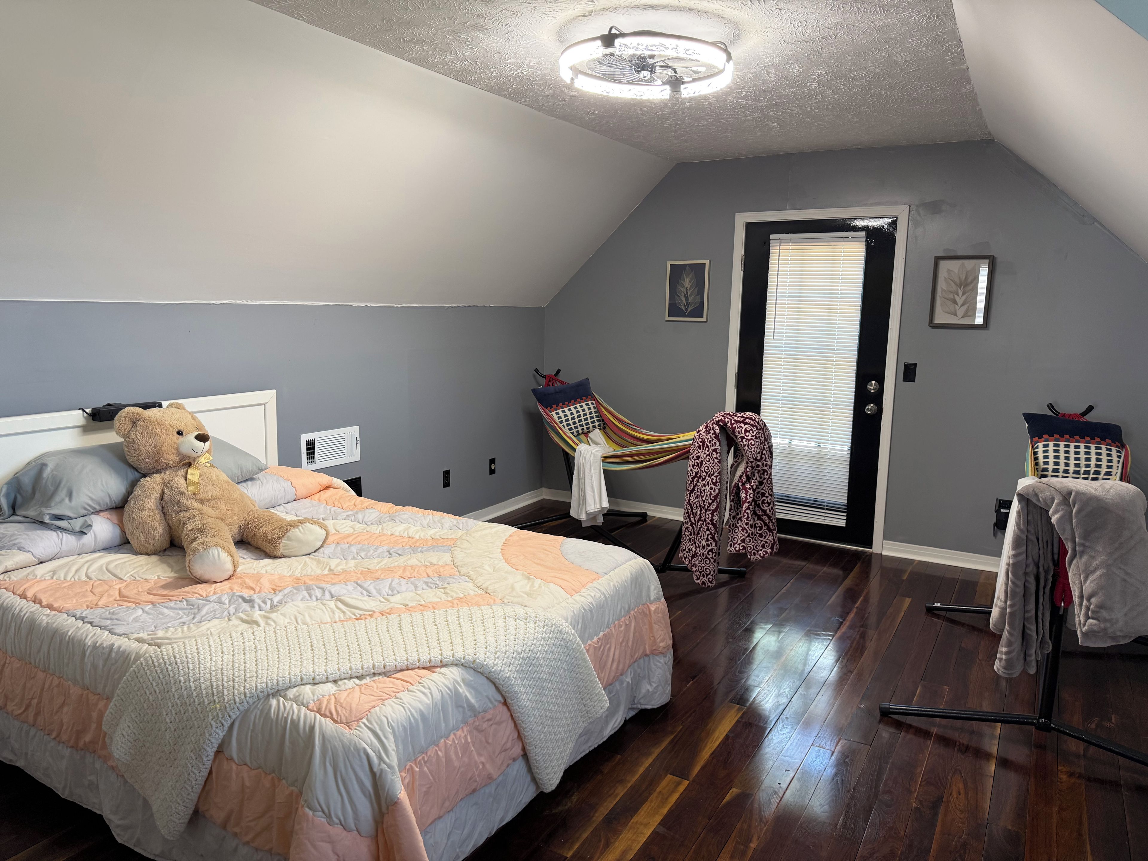 Un dormitorio con una cama grande, un oso de peluche, una hamaca y una puerta con persianas.