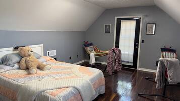 Un dormitorio con una cama grande, un oso de peluche, una hamaca y una puerta con persianas.