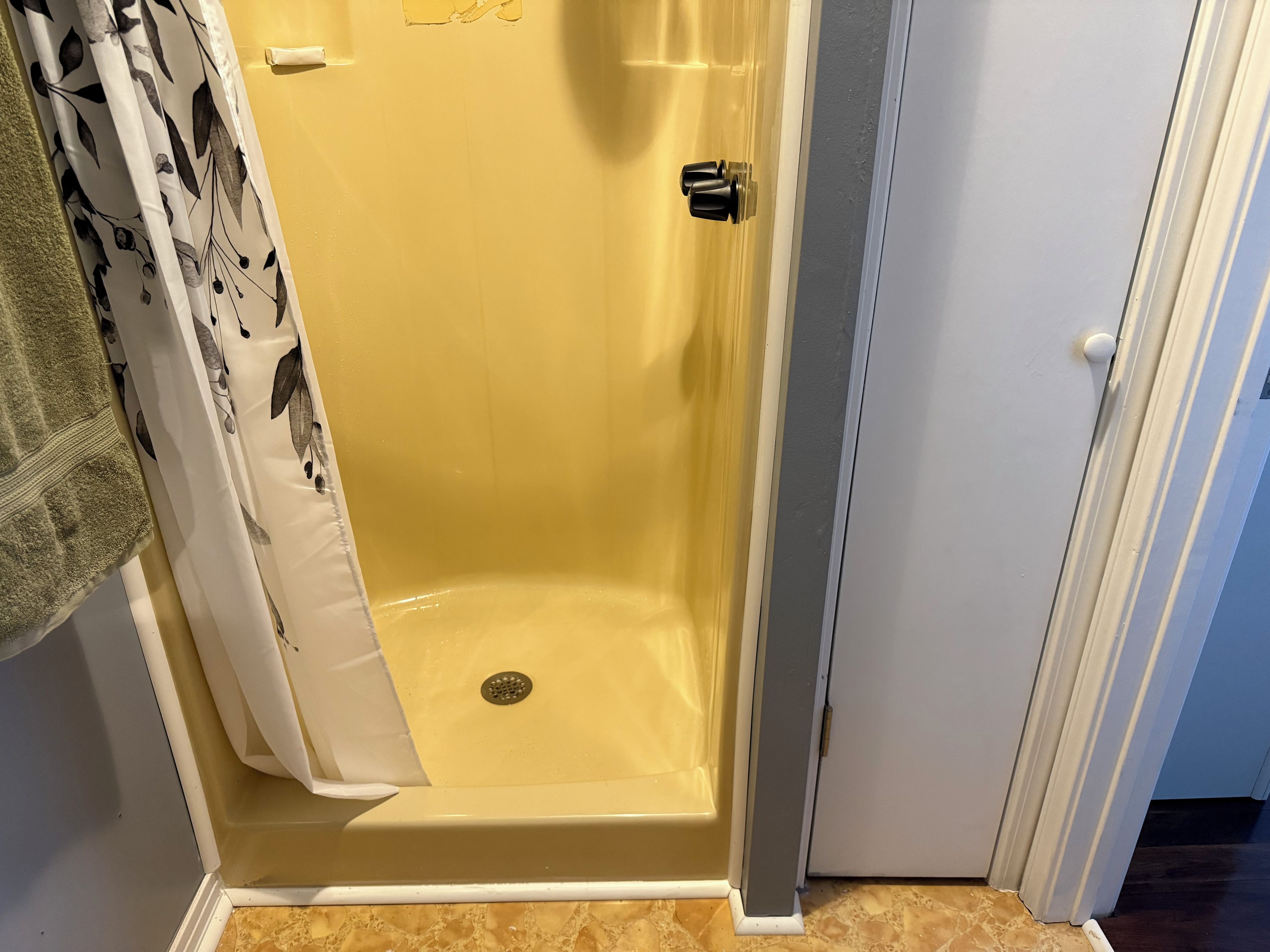 A bathroom with a shower enclosure, a towel rack, and a door.
