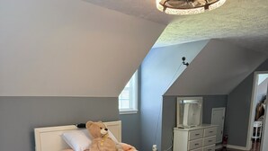 Een slaapkamer met een bed, een groot knuffelbeer, een nachtkastje, een dressoir en een plafondventilator.