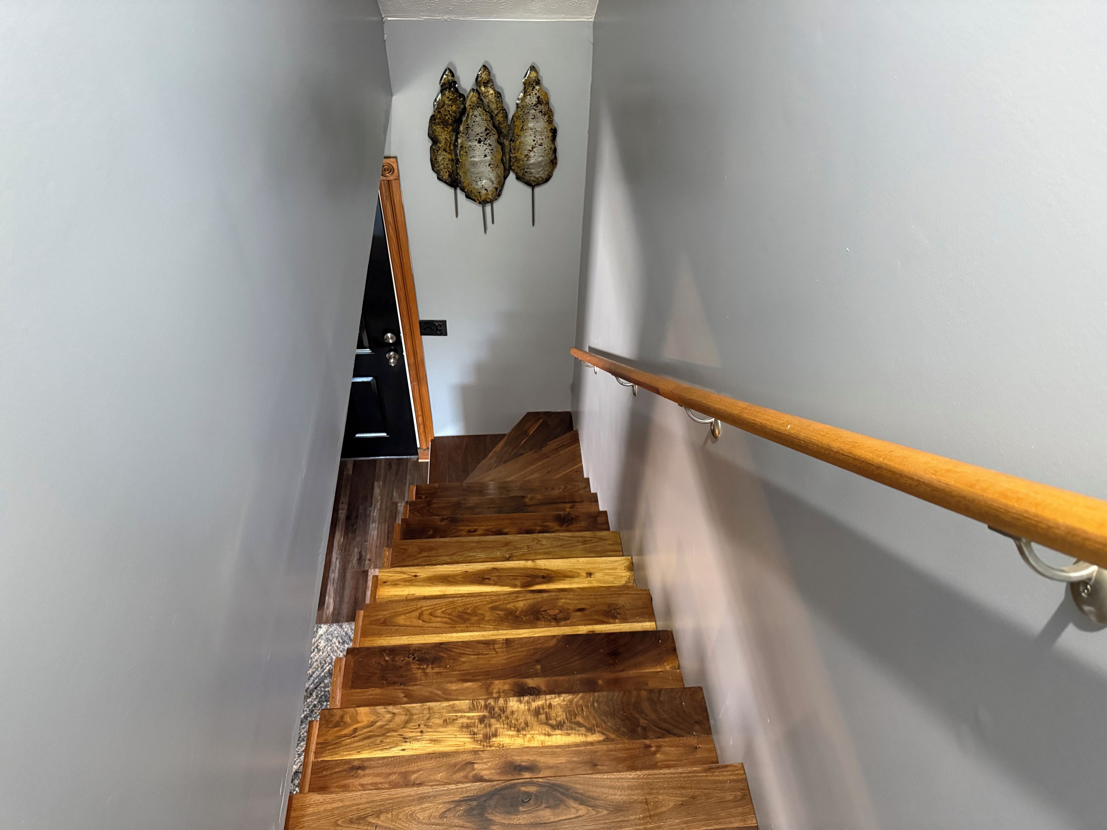 Una escalera de madera con barandilla, una puerta con picaporte negro y un interruptor de luz en la pared.