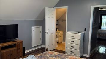 Un dormitorio con cama, televisor, cómoda y ventilador de techo.