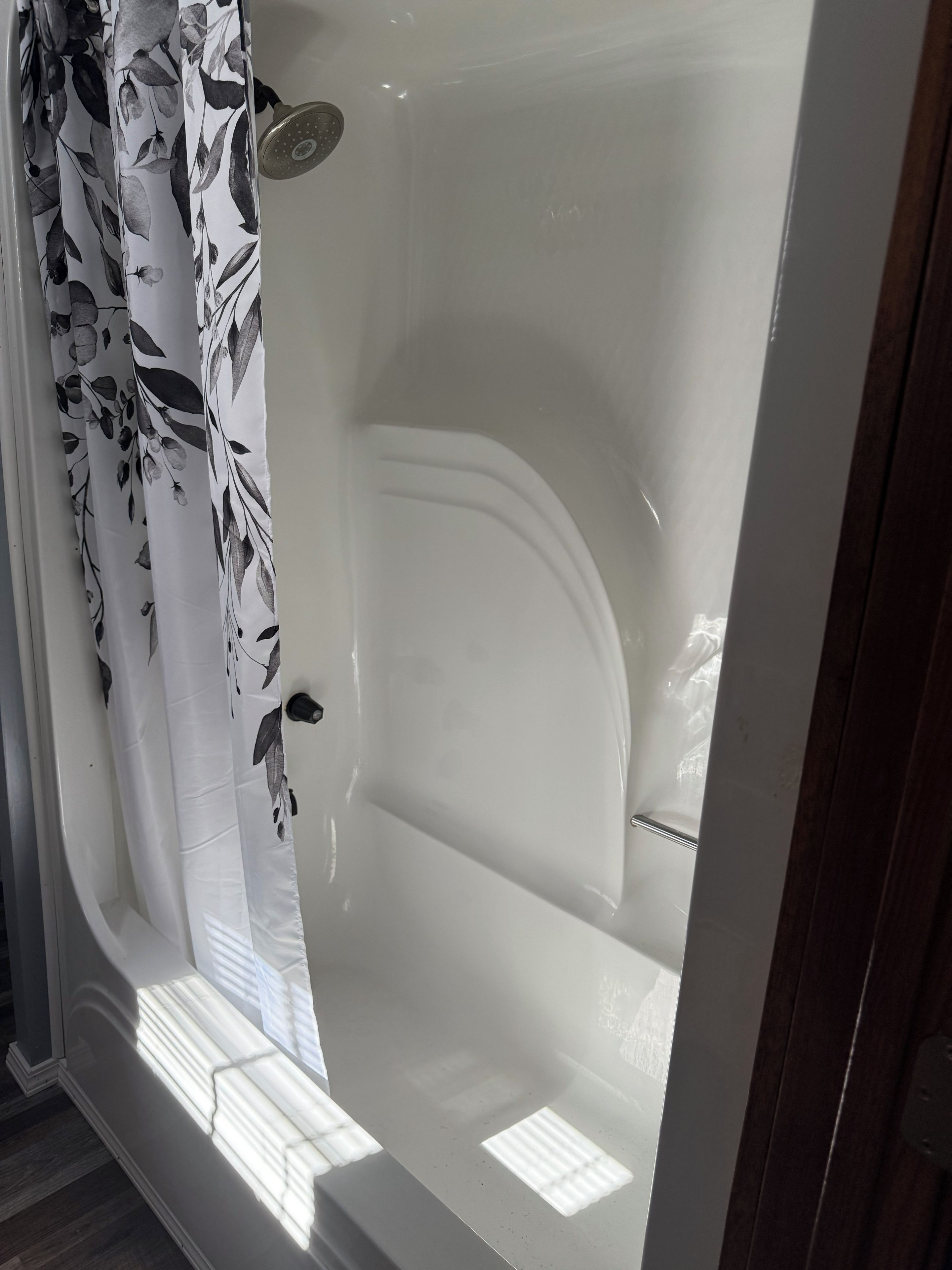 Una bañera con un cabezal de ducha, una cortina con estampado de hojas y suelo de madera.