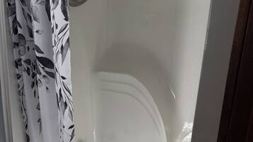 Una bañera con un cabezal de ducha, una cortina con estampado de hojas y suelo de madera.