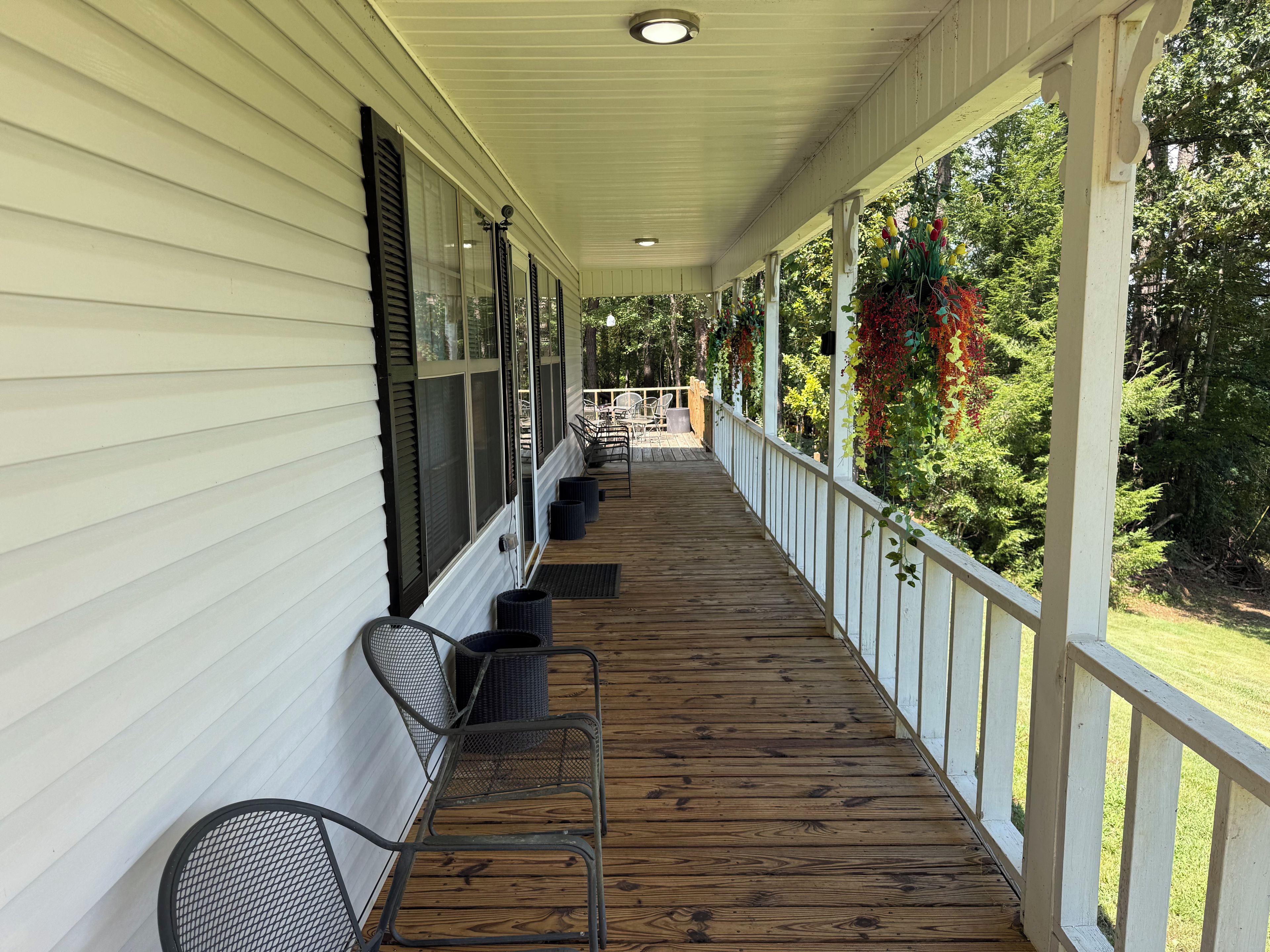 A covered porch with a wooden floor, white railings, and a row of chairs.
