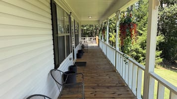 A covered porch with a wooden floor, white railings, and a row of chairs.