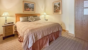 Een hotelkamer met een bed, twee nachtkastjes met lampen, een houten hoofdeinde en twee afbeeldingen in lijsten aan de muur.