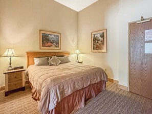 A hotel room with a bed, two bedside tables with lamps, a wooden headboard, and two framed pictures on the walls. - Grand Lodge Studio 176— Walk to Ski Lifts, Pool, Hot Tub (Crested Butte)
