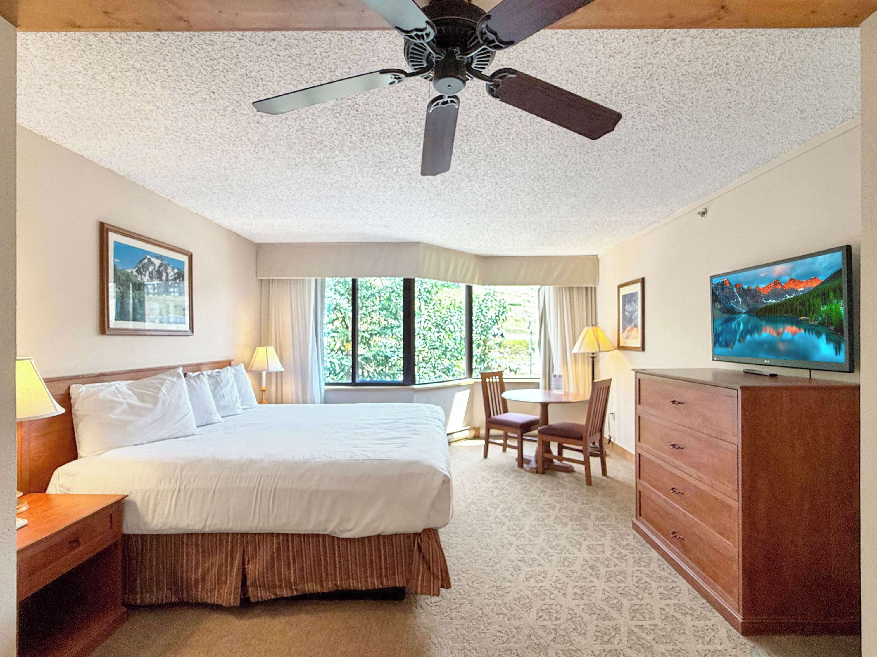 Une chambre d’hôtel équipée d’un lit, d’un bureau, d’une chaise, d’une télévision et d’un ventilateur de plafond.