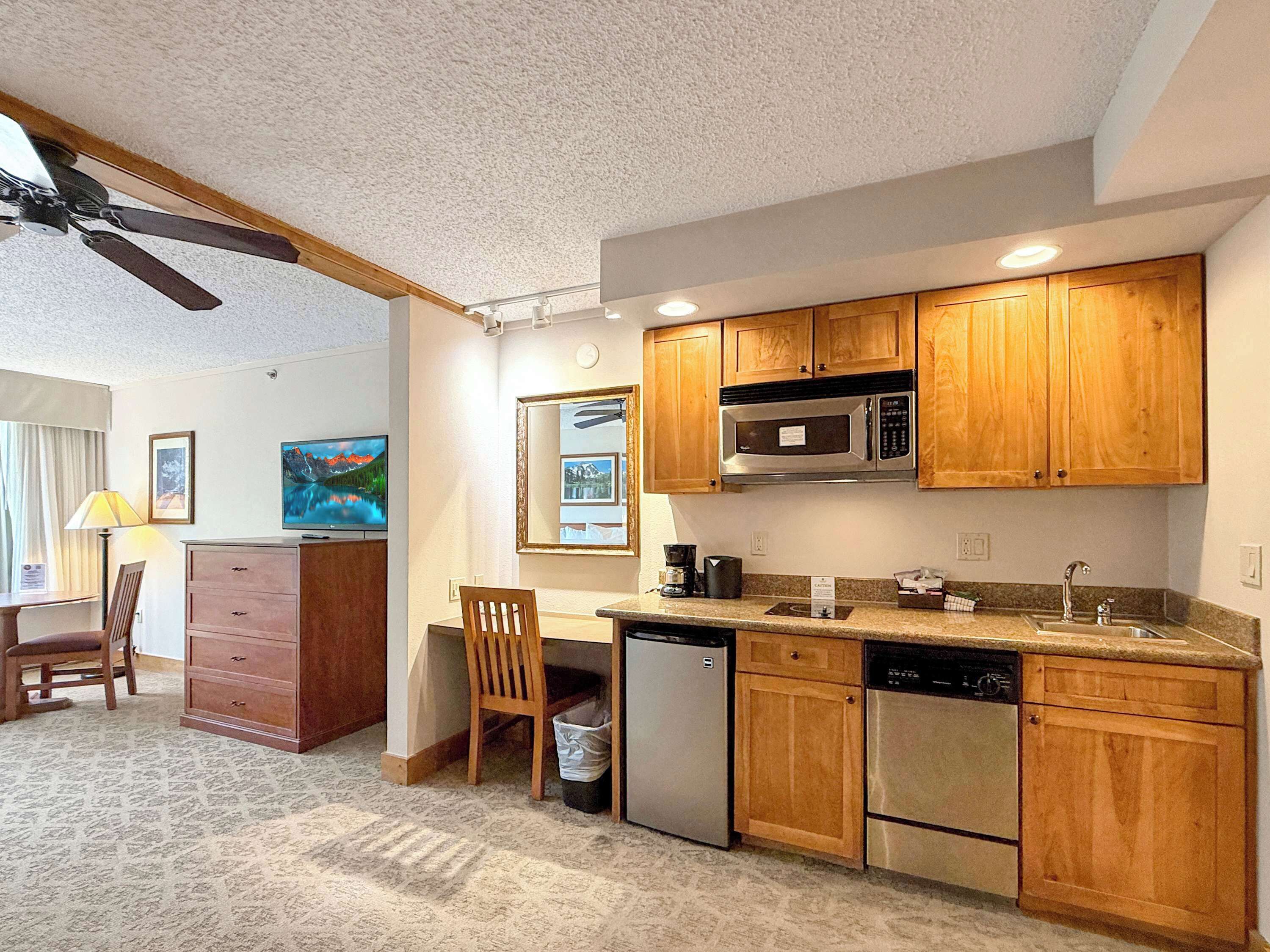 A compact kitchen with wooden cabinets, a microwave, a coffee maker, and a dishwasher.