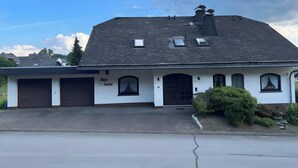 Ein zweistöckiges Haus mit Garage, Schornstein und einem kleinen Fenster mit Vorhang.